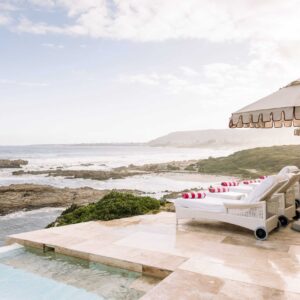 Loungers and umbrellas on the terrace at Birkenhead House above the rocky Walker Bay shoreline at Voelklip, Hermanus