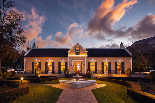 The Cape Dutch manor house at Grande Roche lit at dusk below the Paarl Rock