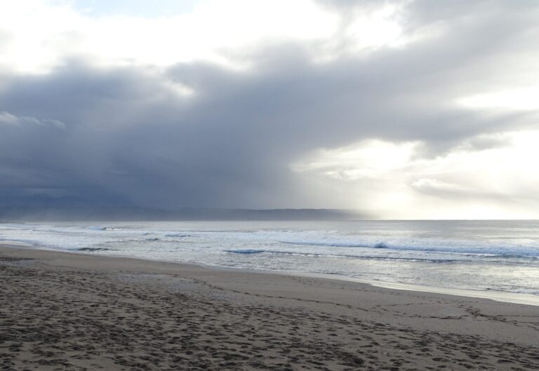 Una amplia playa vacía en Plettenberg Bay bajo un cielo con nubes, con las olas subiendo por la arena