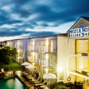 Protea Hotel Knysna Quays lit at dusk beside the Knysna lagoon and marina