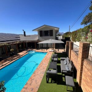 A swimming pool with chairs and an umbrella next to a house at 18 On Louvre Guesthouse in Paarl