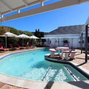 A swimming pool with tables and chairs and a house at 19th Hole Guest Lodge in Hermanus