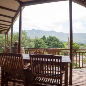 A porch with a table and chairs and mountains at Aan de Bergen in Swellendam