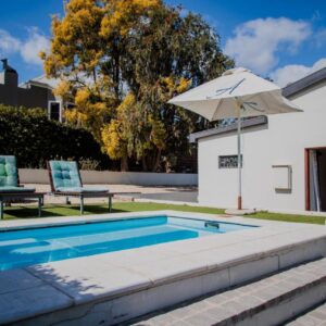 A swimming pool with two chairs and an umbrella at Aan de Heuvel Self-Catering Cottages in Swellendam