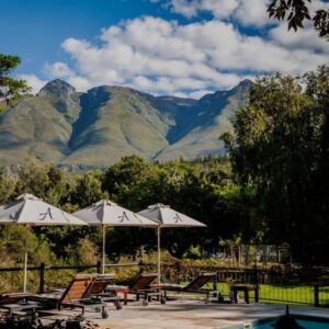 A patio with chairs and umbrellas with mountains in the background at Aan de Oever Guesthouse in Swellendam