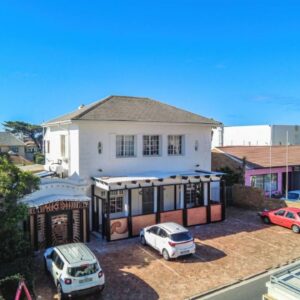 A white house with cars parked in a parking lot at Adamastor Backpackers in Muizenberg