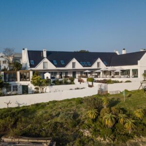 A large white house on the beach with palm trees at Adventure Pad's by The Farmhouse Hotel in Langebaan
