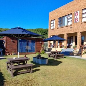 A patio with picnic tables and umbrellas in front of a building at After8 B&B in Kleinbaai