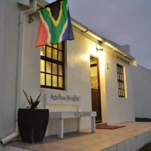 A white cottage with a South African flag and a welcome bench at Agulhas Heights self-catering cottages in Agulhas