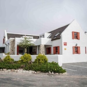 A white building with red windows and a parking lot at ah! Guest House in Paternoster
