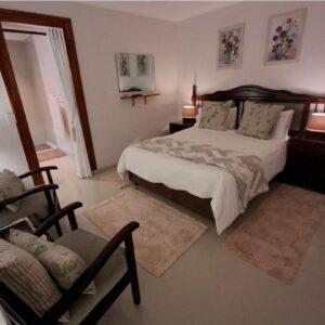 A bedroom with a bed and two chairs and two lamps at Alikreukel Accommodation in Plettenberg Bay