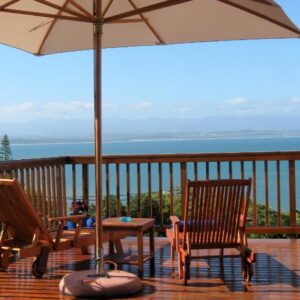 A patio with two chairs and an umbrella on a deck at Aquamarine Guest House in Mossel Bay