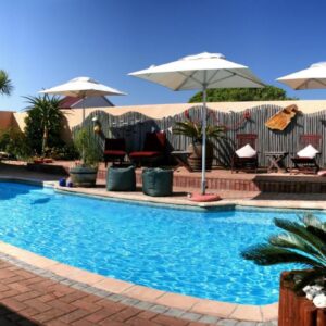 A swimming pool with umbrellas and tables and chairs at Avenues Guesthouse in Mossel Bay