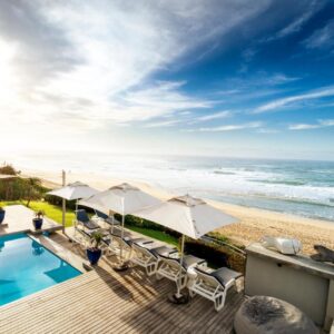 A swimming pool with umbrellas and the beach at Beach Villa Wilderness in Wilderness