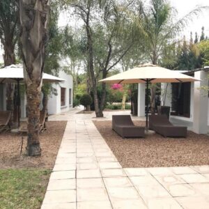 A patio with two umbrellas and chairs and trees at Blue Mountain View Cottages in Clanwilliam