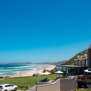 A view of a beach with cars parked in front of a building at Brenton Haven Beachfront Resort in Knysna