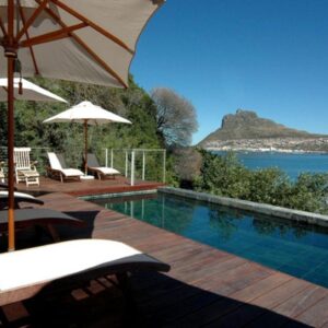 A swimming pool with chairs and umbrellas and the ocean at Chapmans Peak Beach Hotel in Hout Bay
