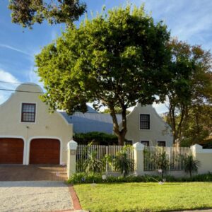 A white house with a white fence and a tree at Chinta Cottage Hermanus in Hermanus