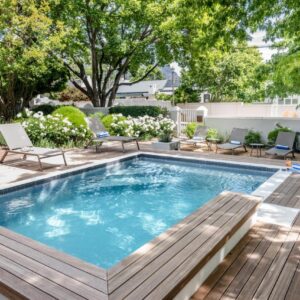 A swimming pool with a wooden deck and chairs around it at Corner House Residence in Franschhoek