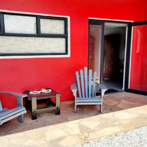 Two chairs and a table in front of a red wall at Die Boom in Lambertʼs Bay