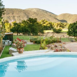 A swimming pool in a garden with mountains in the background at Die Fonteine Country Guesthouse and Glamping in Oudtshoorn
