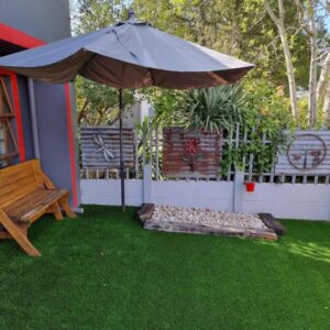 A patio with an umbrella and a bench and grass at Dolphins Self-Catering Accommodation in George