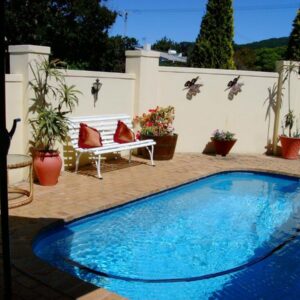 A swimming pool in a patio with a bench and potted plants at DOTJJ B & B in Paarl