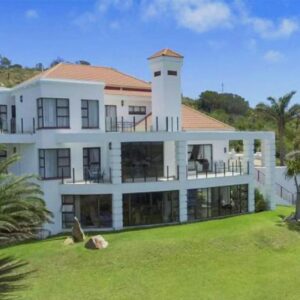 A large white house on top of a lush green field at Fly Me To The Moon Guesthouse in Mossel Bay
