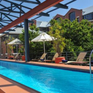 A pool with chairs and umbrellas next to a building at Garden Court Victoria Junction in Cape Town