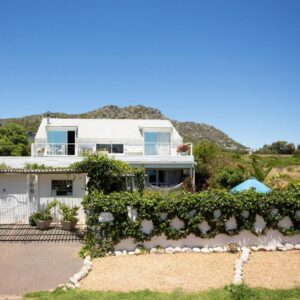 A white house with a fence and bushes at Guinea Fowl House in Kommetjie