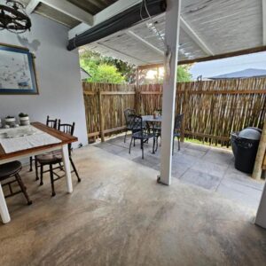 A patio with a table and chairs and a fence at Heide Cottage in Struisbaai