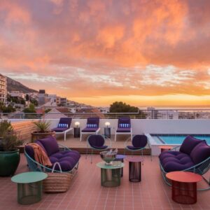 A rooftop deck with chairs and tables and a sunset at Home Suite Hotels Sea Point in Cape Town