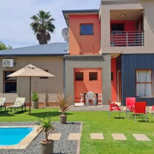 A house with a swimming pool and chairs and umbrellas at Karoo Sun Guest House in Oudtshoorn
