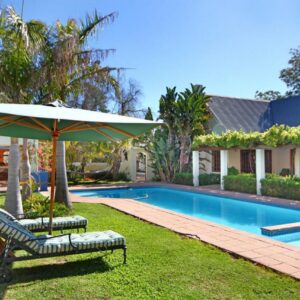 A pool with two chairs and an umbrella next to a house at Kleinbosch Lodge in Stellenbosch