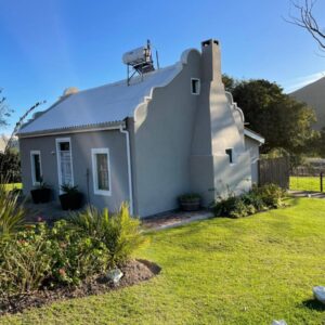 A small white house with a grass yard at Kleine Vrede Farm Cottage in Hermanus