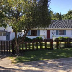 A white house with a fence and a tree at Knysna Holiday Cottage in Knysna