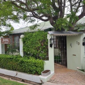 A white house with a gate and a tree at Knysna Self Catering Accommodation in Knysna