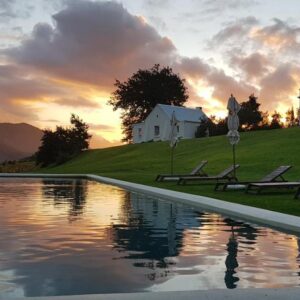 A pool in front of a house with a sunset at La Cotte Forest Cottages in Franschhoek