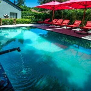 A swimming pool with red chairs and umbrellas at La Fontaine Boutique Hotel by The Oyster Collection in Franschhoek