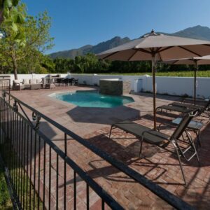 A patio with chairs and an umbrella and a pool at La Galiniere Guest Cottages in Franschhoek