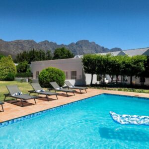 A swimming pool with chairs and a house at La Jolie Dauphine Guest House in Franschhoek