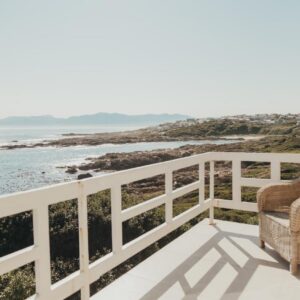 A chair on a balcony looking out at the ocean at La Melamire On the Rocks Bed & Breakfast in Gansbaai