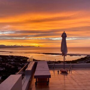 An umbrella and a table on a balcony with a sunset at La Vista Lodge in Plettenberg Bay