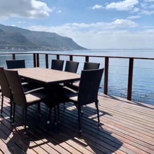 A wooden deck with a table and chairs next to the water at Lalapanzi in Fish hoek
