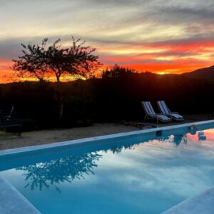 A swimming pool with a sunset in the background at Le Petit Karoo in Oudtshoorn