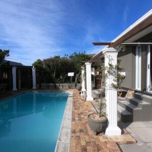 A swimming pool next to a house with a potted plant at Leo's Den in Fish hoek