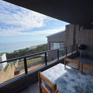 A balcony with a table and a view of the ocean at Lilies & Leopards B&B in Mossel Bay