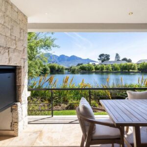 A covered terrace with a fireplace and dining table looking over the lake at Luxury Lodge 5B, Pearl Valley Golf Estate