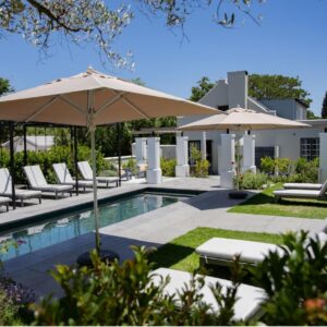 A pool with chairs and umbrellas next to a house at Macaron Boutique Guest House in Franschhoek