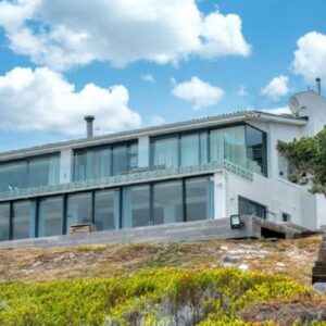 A white house with glass windows on top of a hill at Marlin Manor in Struisbaai